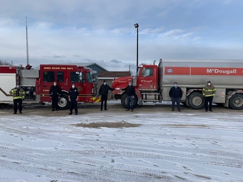Owen Sound Fire Fighters Get $5,000 from McDougall Energy Towards Christmas Toy Drive 91 Shows a shot of 7 people outdoors winter with a firetruck and a McDougall fuel truck behind them