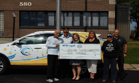 Shows 6 people outside holding a large cheque from McDougall Energy