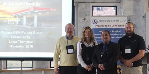 Shows 4 people standing smiling standing in from of a projection screen