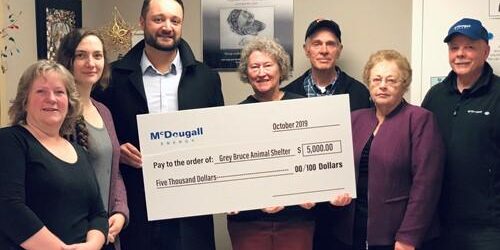 Shows 7 people inside house holding a large cheque from McDougall Energy