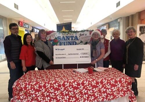 Shows 7 people standing in a shopping mall holding a large cheque from McDougall Energy during Christmas