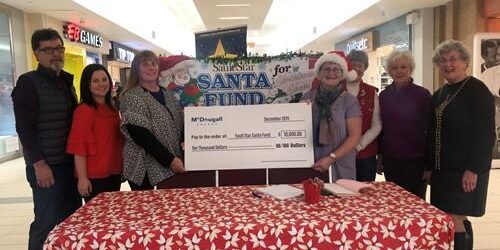 Shows 7 people standing in a shopping mall holding a large cheque from McDougall Energy during Christmas