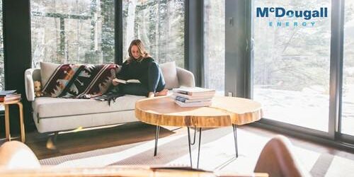 Shows a woman reading a book sitting on a large couch in a large room surrounded by windows