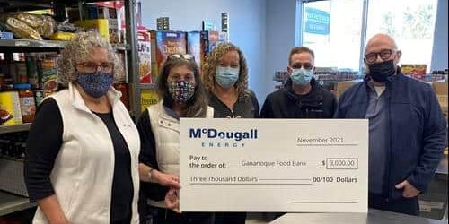Shot of 5 people standing indoors at a food bank wearing face masks holding a large cheque from McDougall Energy
