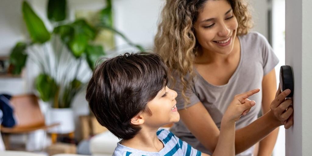 Child and mother interacting with a smart thermostat device.
