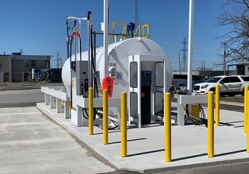 Show outside shot of large stationary fuel tank and yellow guard posts surrounding it