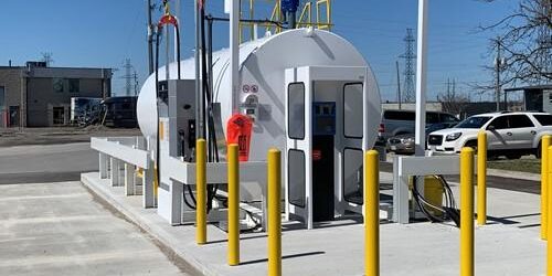 Show outside shot of large stationary fuel tank and yellow guard posts surrounding it