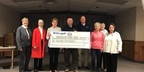Shows 8 people on a stage holding a large cheque from McDougall Energy