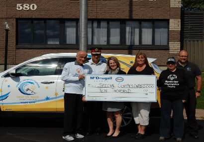Shows 6 people outside holding a large cheque from McDougall Energy
