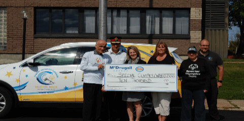 Shows 6 people outside holding a large cheque from McDougall Energy