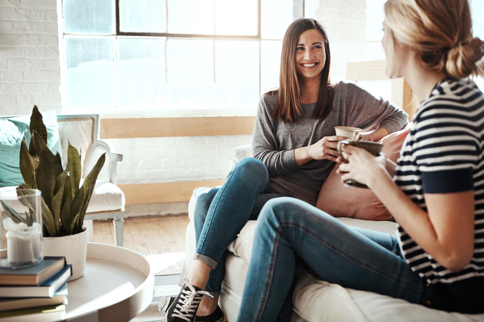 Shot of two women having coffee and chatting while sitting in a living room